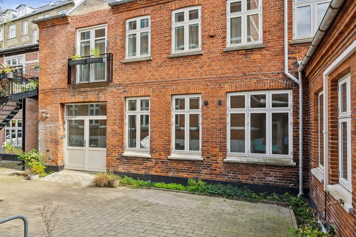 En smuk gård med røde mursten og hvide rudevindue, og en stor åben dør til værkstedet