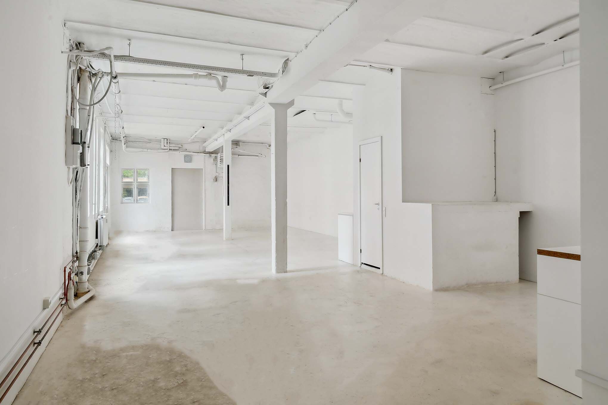 Ren, hvid og renset værksted med højloft og store vinduer på den ene side og høj loftsstrukturer på den anden side