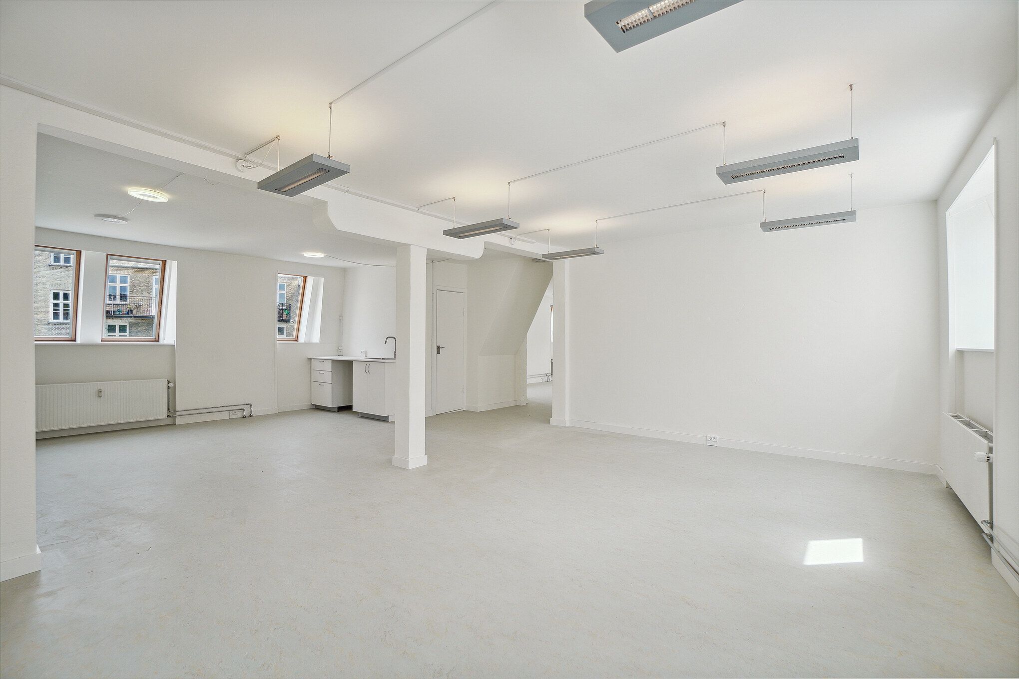 En stor, lys, møbleret lejlighed med hvide vægge, loft og gulv samt store vinduer og højloftede rum.