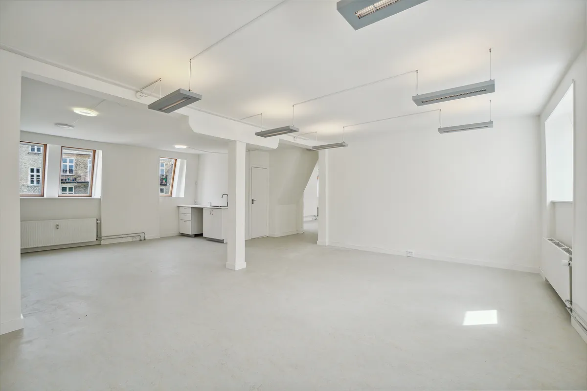 En stor, lys, møbleret lejlighed med hvide vægge, loft og gulv samt store vinduer og højloftede rum.