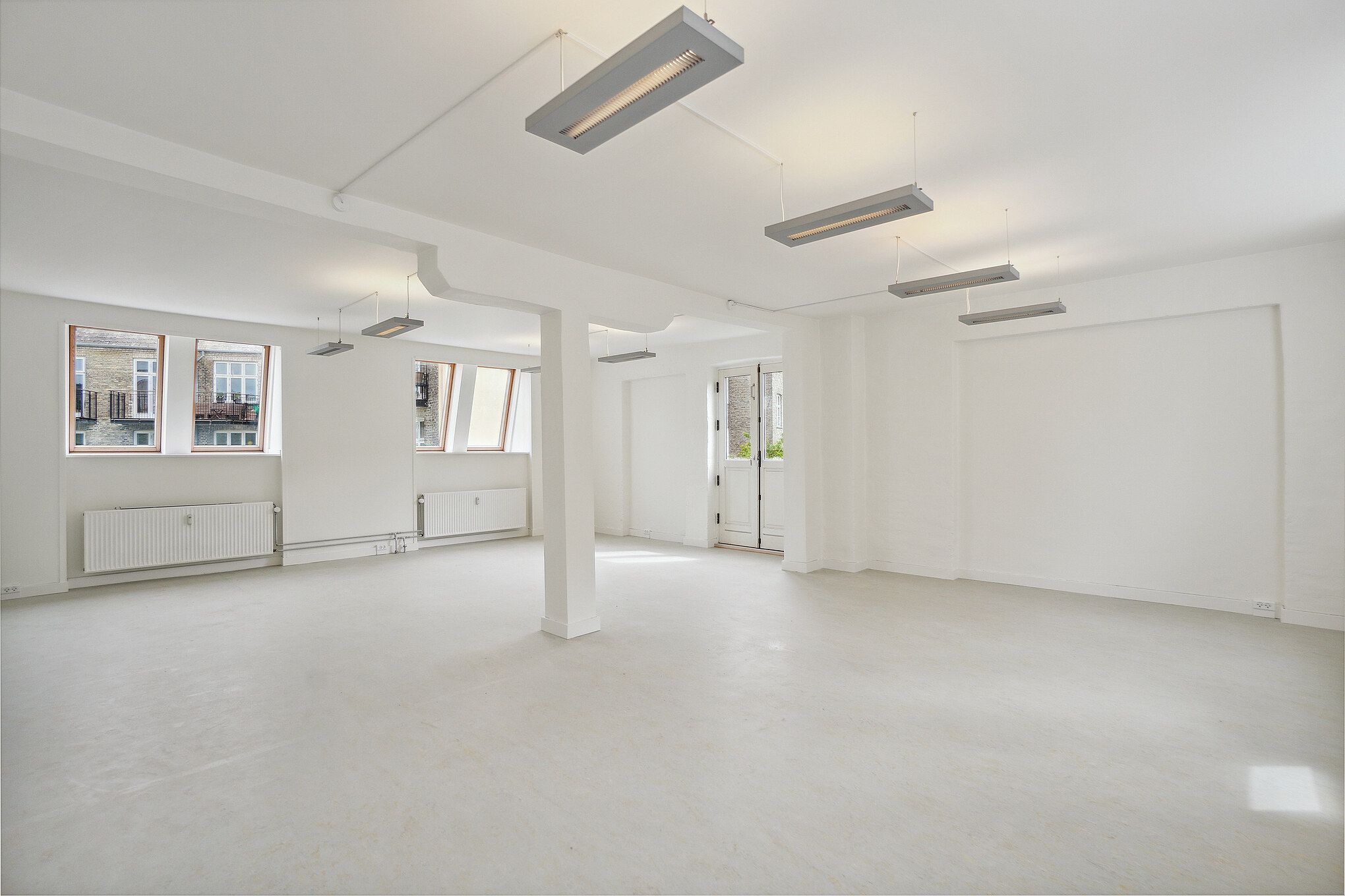 Lyst og attraktivt lejemål med hvide vægge og loft. Store vinduer og lyse armaturer. Høj loftshøjde og højt loft.