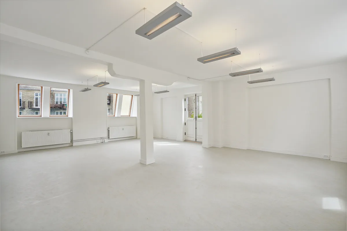 Lyst og attraktivt lejemål med hvide vægge og loft. Store vinduer og lyse armaturer. Høj loftshøjde og højt loft.