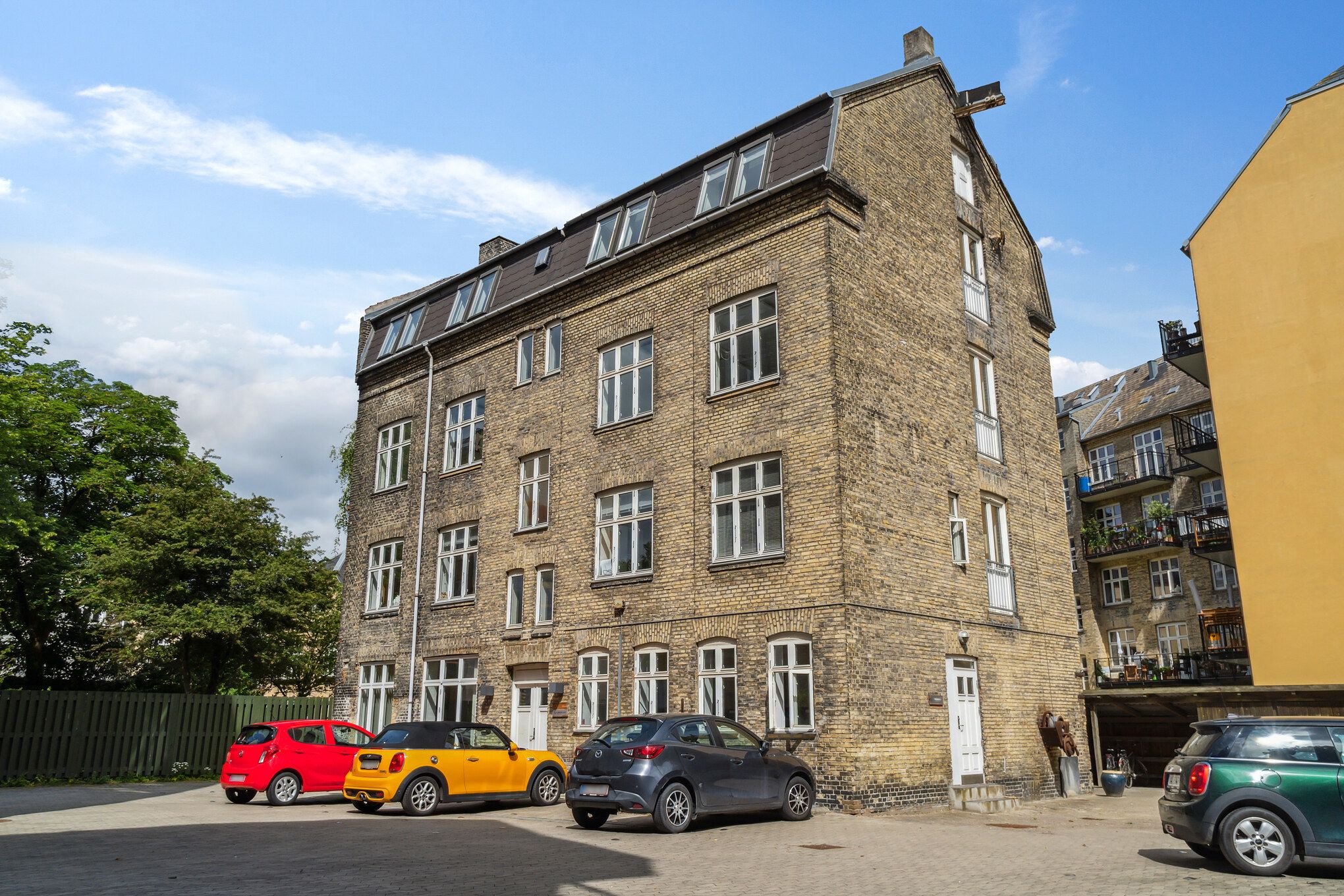 Lejlighedshus med fem parkerede biler, hvoraf to er Mini Coopers, og tre er andre små biler i forskellige farver, samt