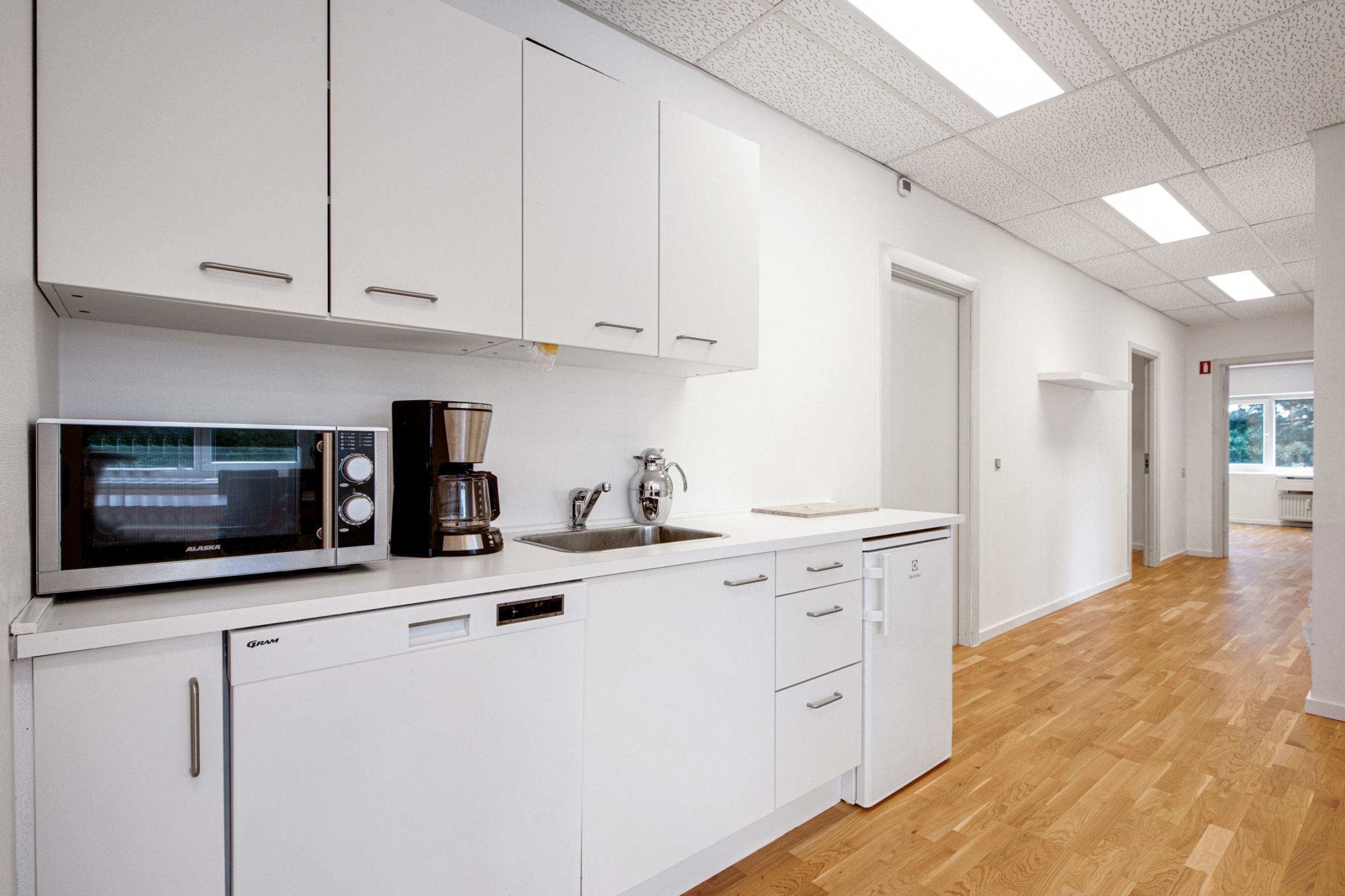 Moderne køkken med hvide skabe og højloftede rum, lyse loftsbelægninger, stående mikroovn og lysegre trægulve