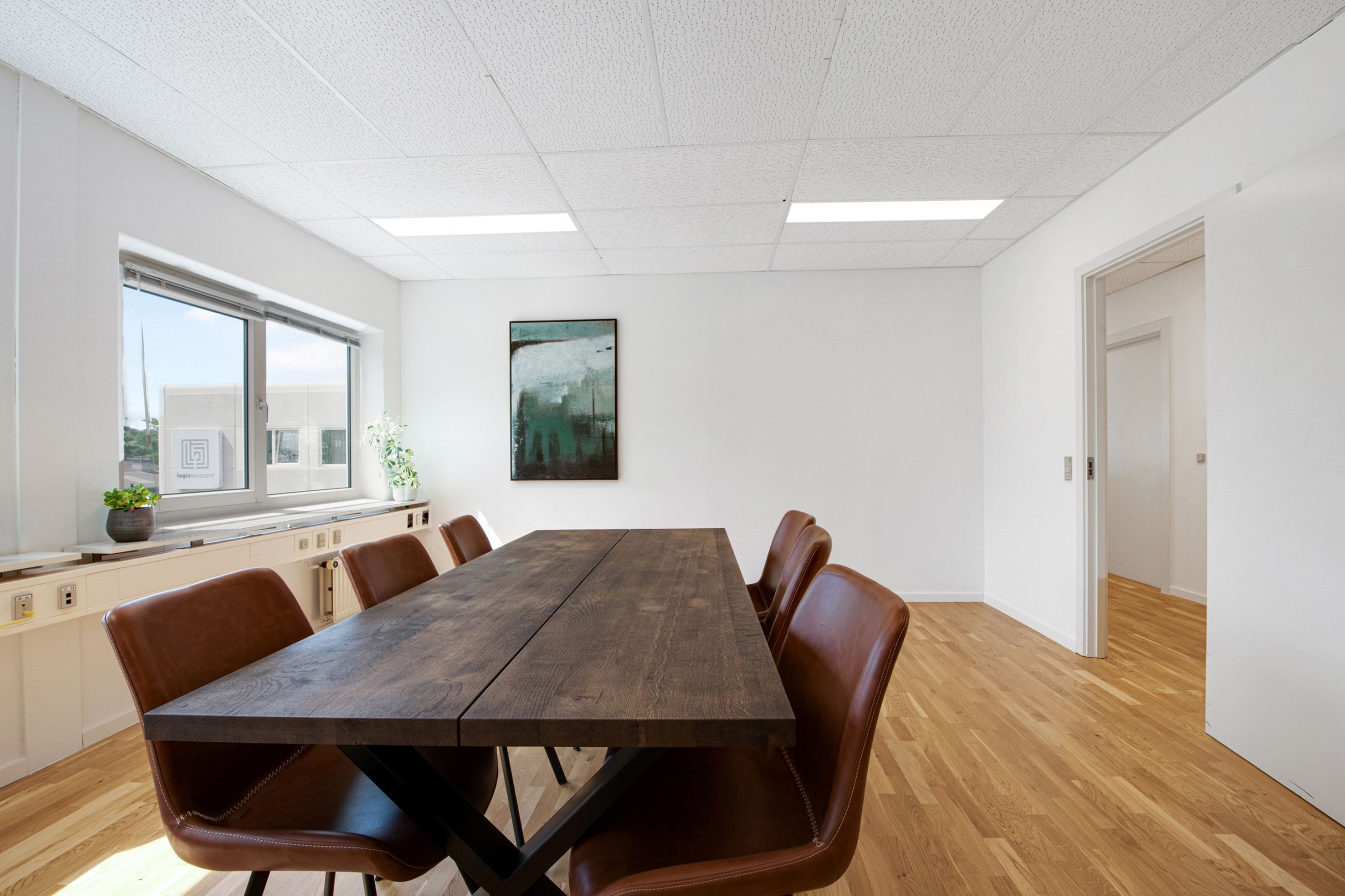 Foto af et tomt kontor med en lang træbord og læderstole samt et kunstværk på væggen