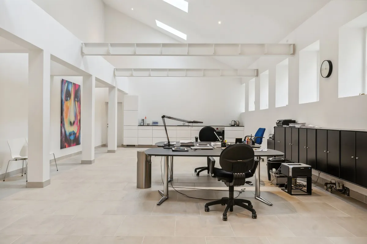 Moderne kontor med højt loft, hvide vægge, lyse gulve og minimalistisk indretning, der inkluderer en stor skrivebord, flere