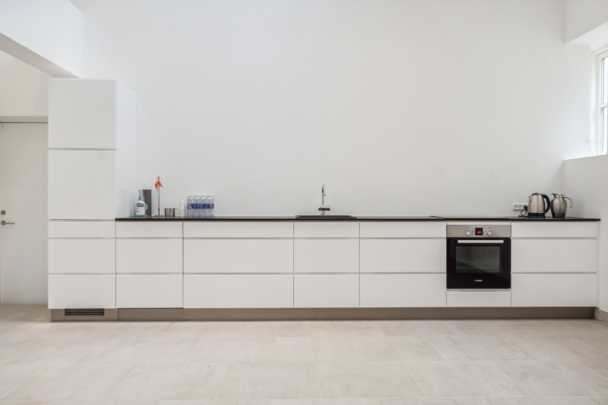 Rent køkken med hvide vægge, hvide køkkenskabe og en høj, slank ovn med digital display