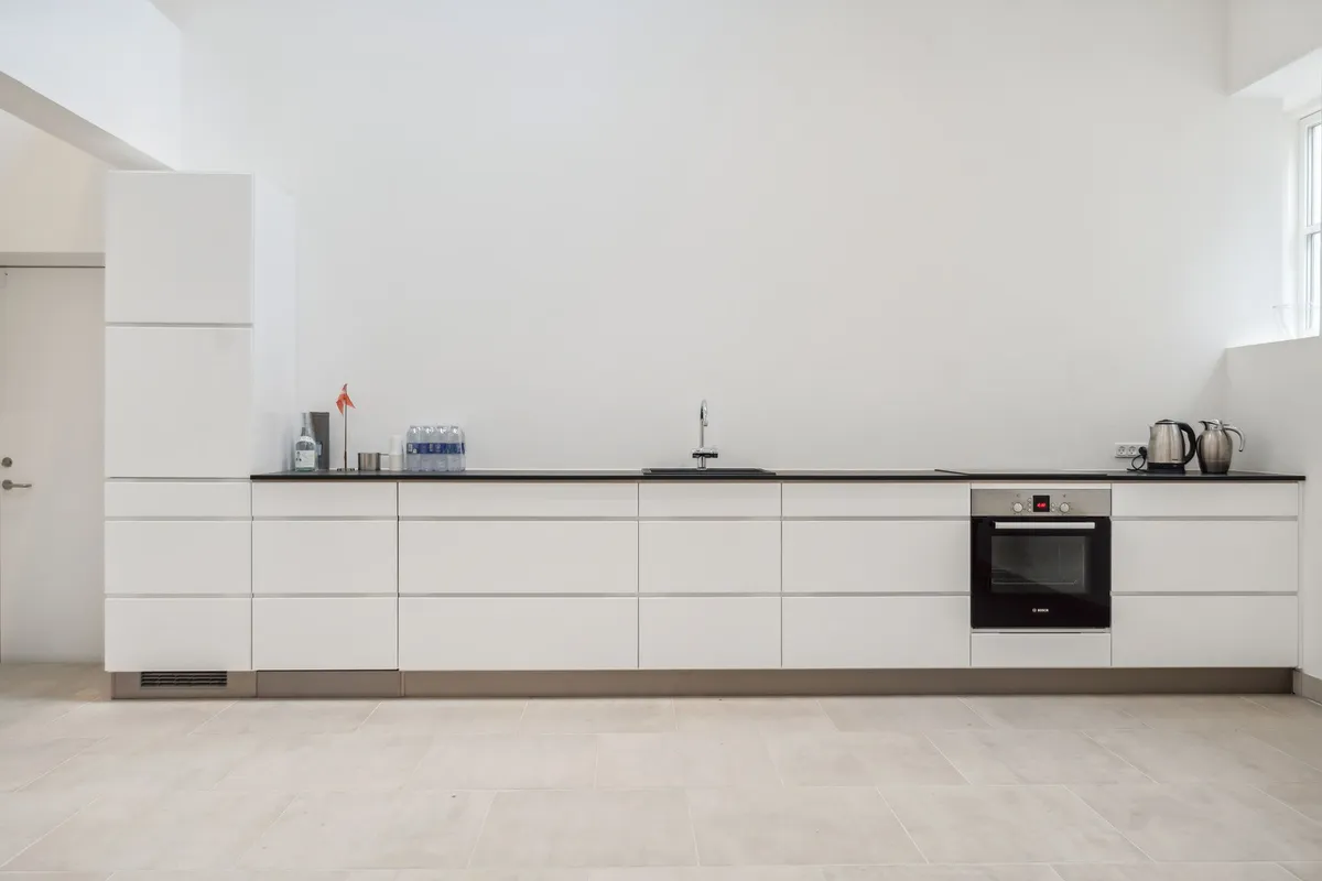 Rent køkken med hvide vægge, hvide køkkenskabe og en høj, slank ovn med digital display