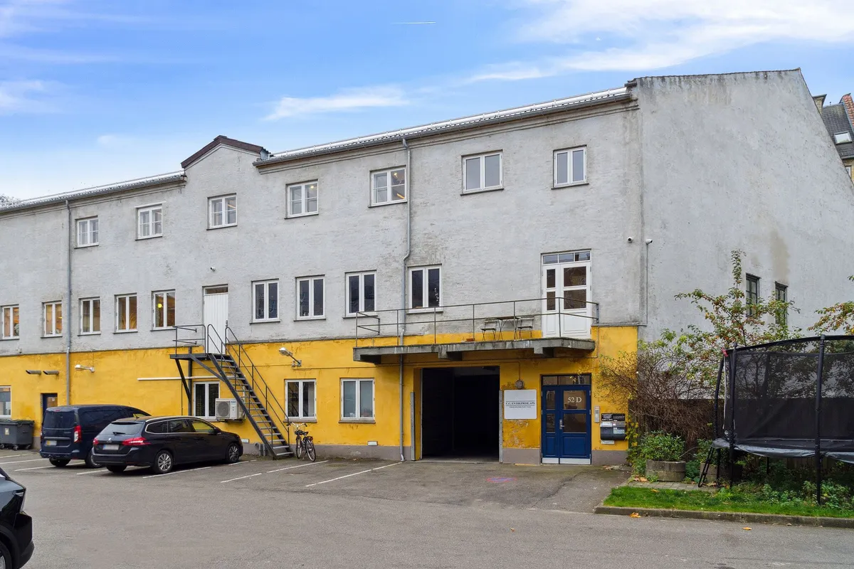 Loft til kip og stor vareelevator til etagen. To biler parkeret i parkeringspladsen. Trampolin og træer ved siden af