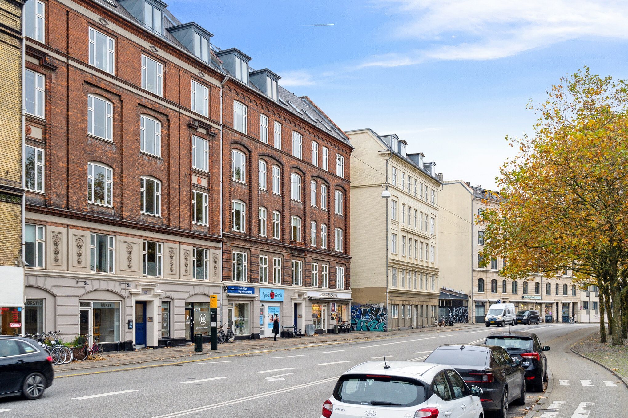 Værksted og showroom på Frederiksgade i København med biler parkeret og mennesker, der går på fortovet og træer og gadebelys