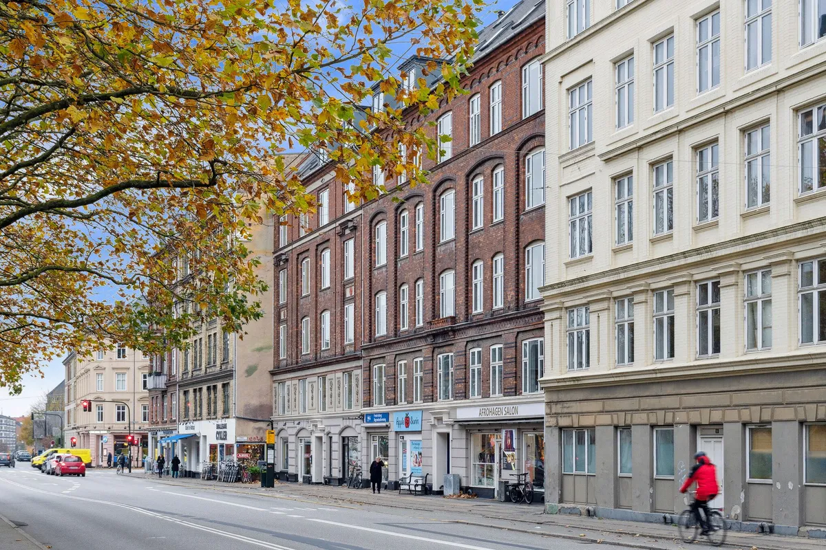 En person cykler forbi et stort rødt bygningskompleks med butikker og kontorer i København med røde teglsten og mange vinduer