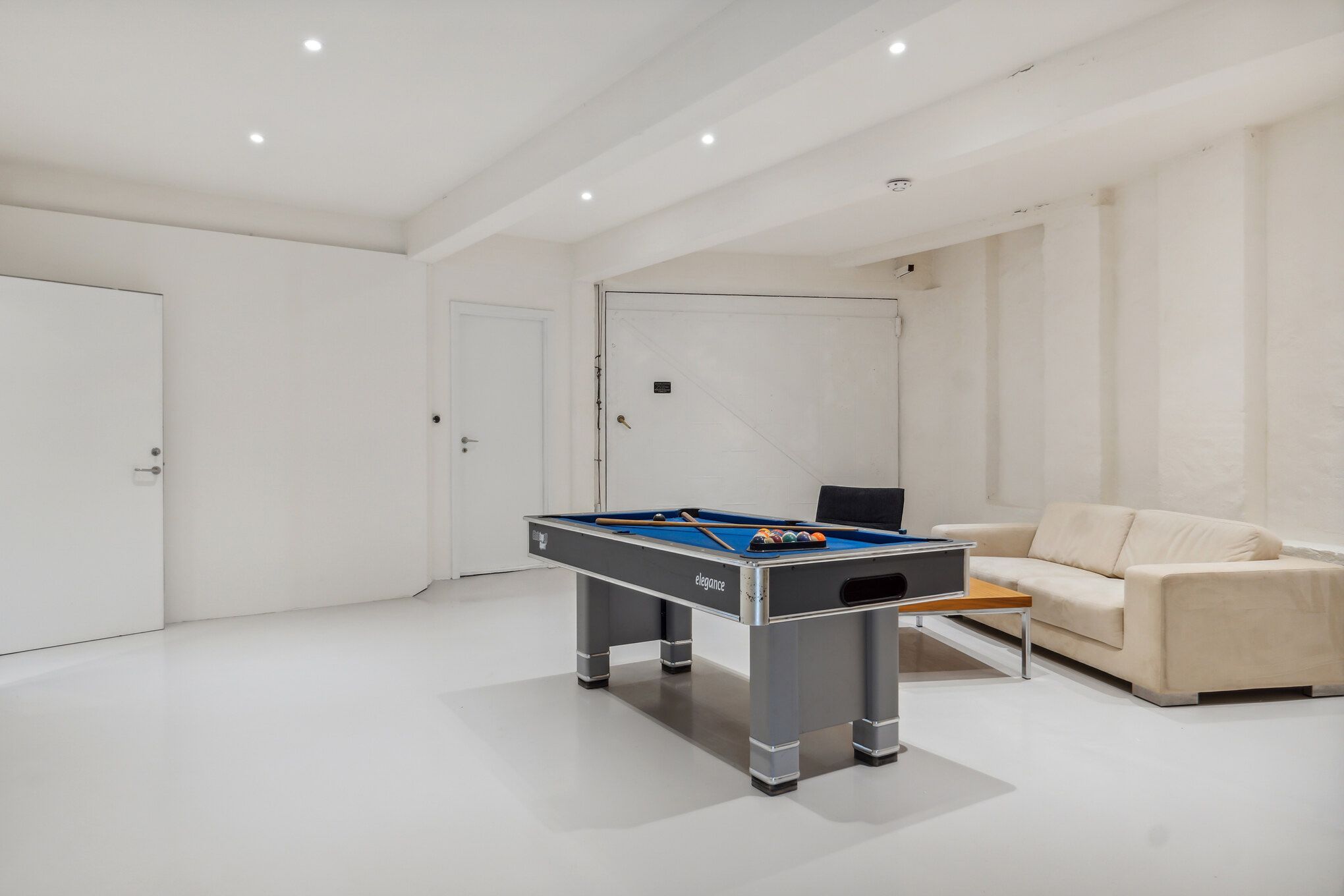 Billardbord i en hvid stue med beige sofa og lyse pletter på loftet og væggen