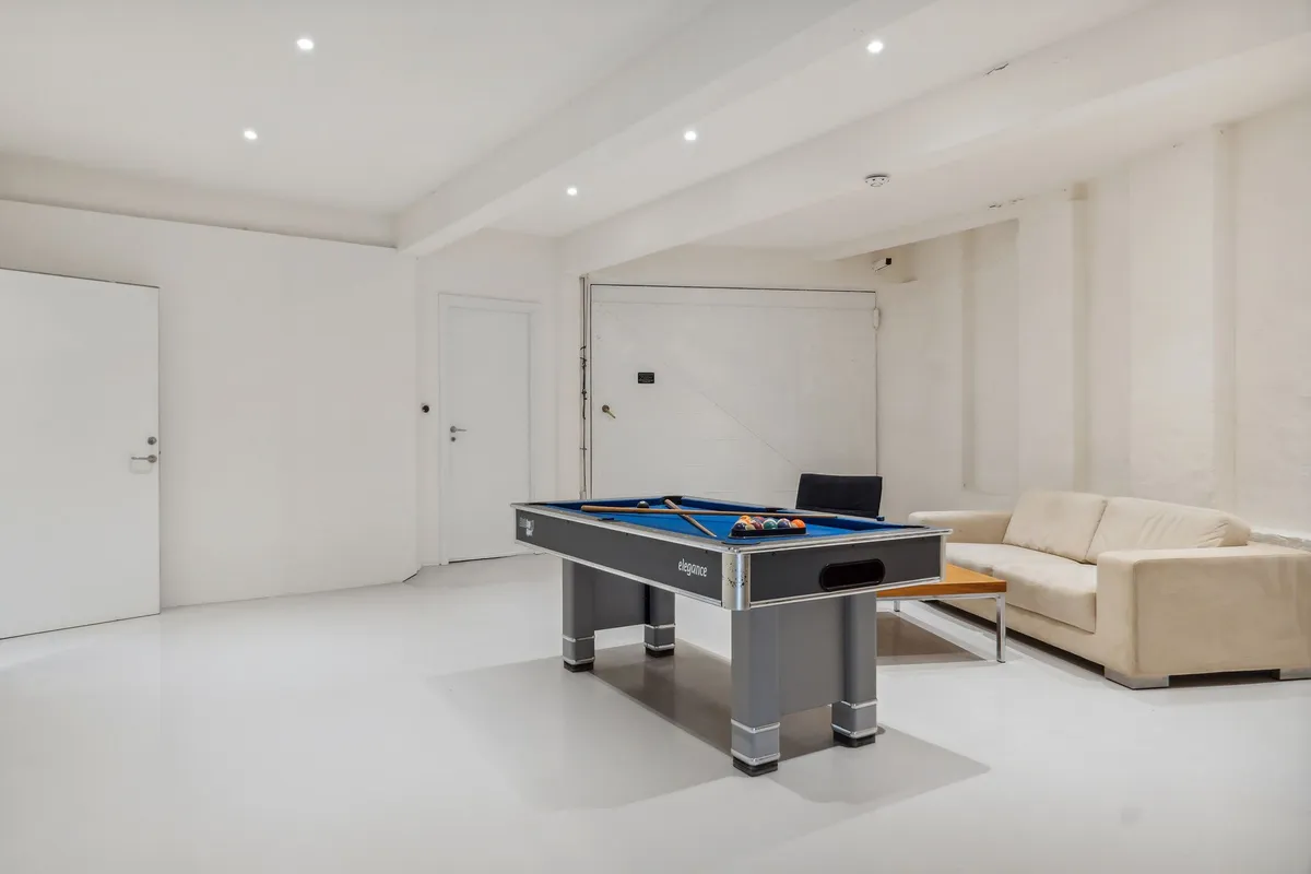 Billardbord i en hvid stue med beige sofa og lyse pletter på loftet og væggen