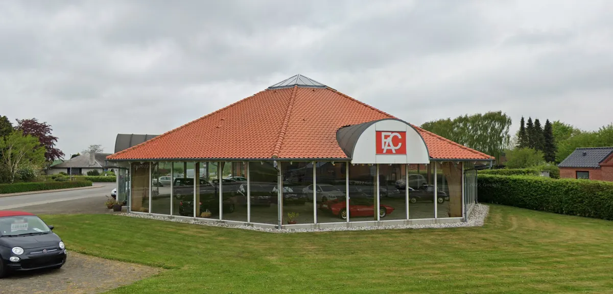 Moderne erhvervslokale med rødt tag og logoet FC, foran parkeret bil, med flere biler og bygninger i baggrunden