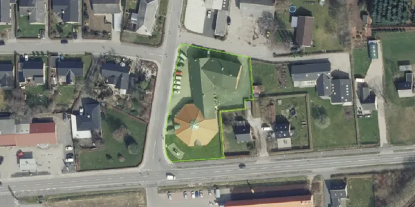 Erhvervsgrund med stort gult pavillon på Svinget 2 i Jelling, omgivet af grønne områder og bebyggelse, med bilparkering og