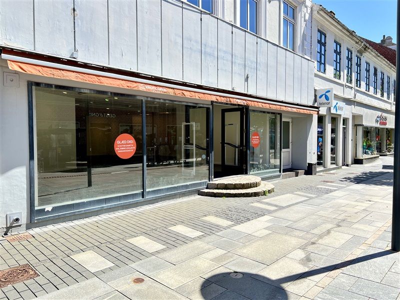 En tom butik med tomme ruder og røde skilte med tekst og nummer 1504. Butikken ligger på en bred og lækker gågade med