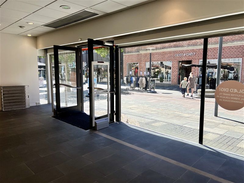 To hvide glasdøre med svart indramning står åbne, og der er en tekst med rabattilbud i en rund skilt.