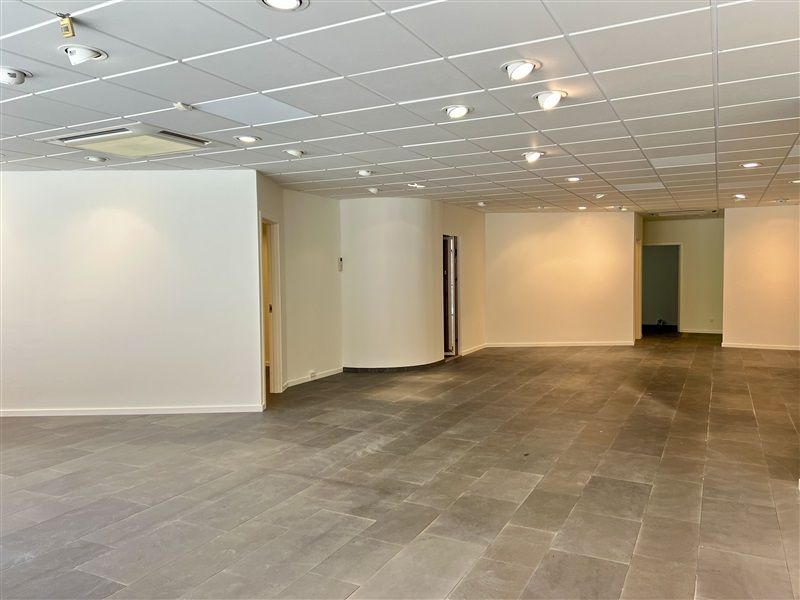 En stor, tom og rummelig kontorlokal med hvide vægge, gulv og loft samt lysekroner og to døre