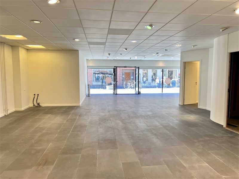 En stor og lys rummelig butikslokale med glasdøre og højloft samt trægulv og lysekroner i loftet