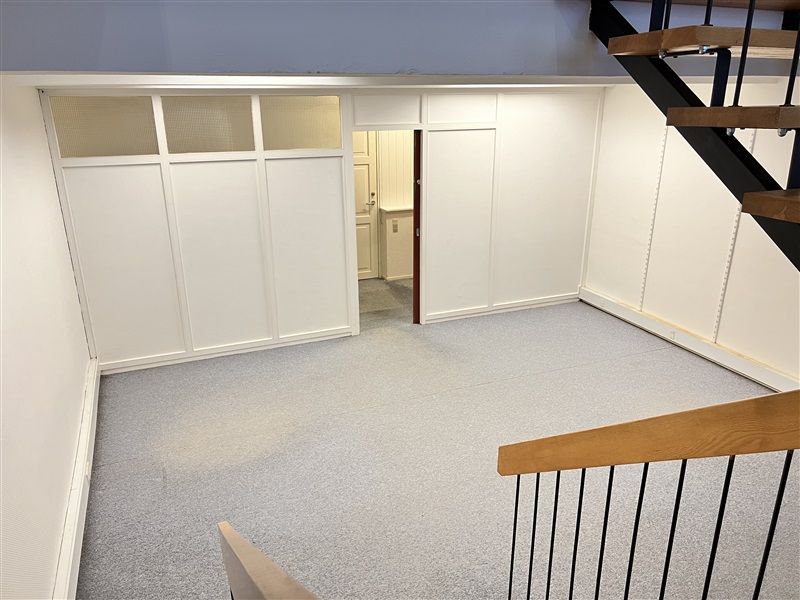 Rum med hvidt panel og gulv. Åbne døre til en stue. Trin med hvide trin og mørke stænger.