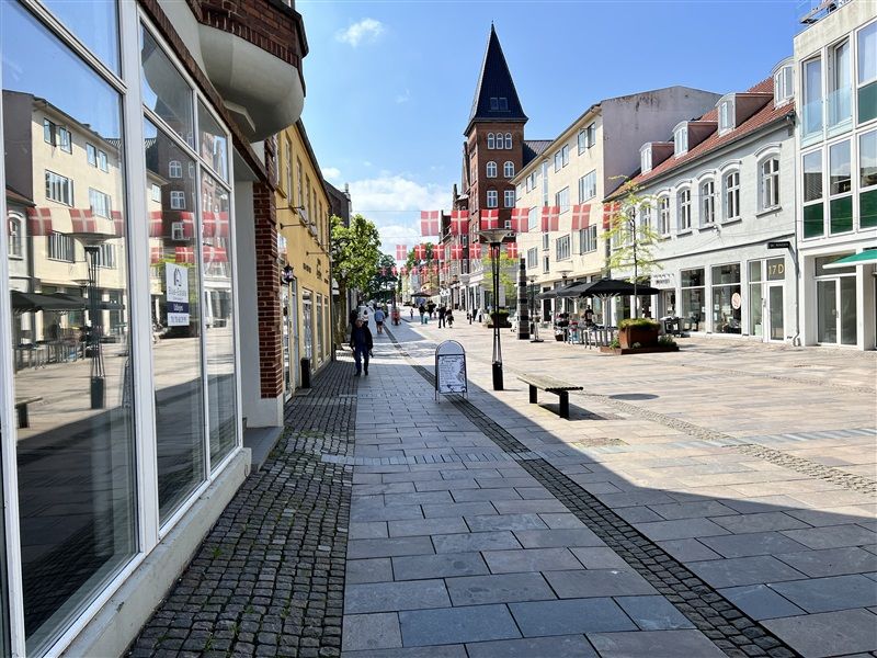 Frederiksgade i Fredericia med gågade, torv, forretninger, bygninger og danske flag på facaderne