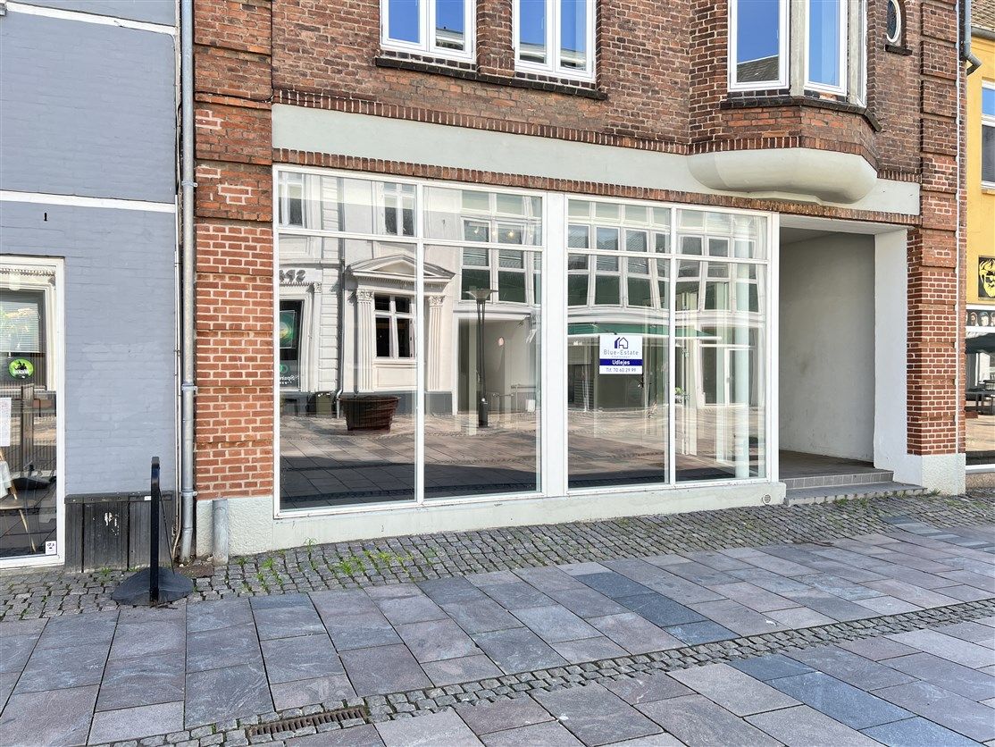 Forretningslokaler med store glasvinduer og højt loft. De lyse glasvinduer reflekterer bygningen og området omkring.