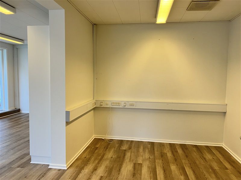 Minimalistisk kontorlokal med hvide vægge, gulv og loft, lysekrone og stikkontakter langs væggen