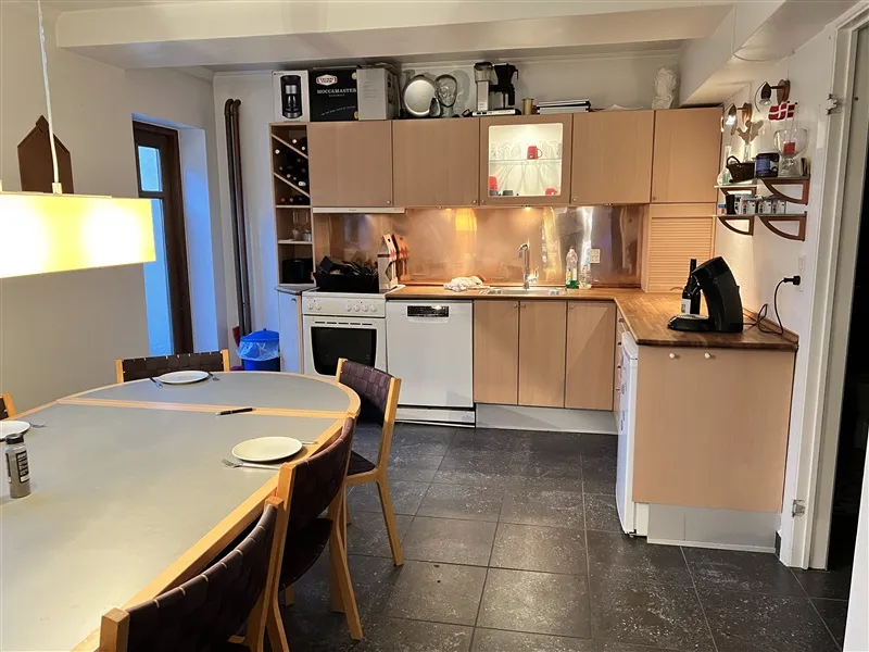 Moderne køkken med lyse nuancer og fuldt udstyret med hvide apparater og lyse egner. Lyskroner og lysepunkter giver et lyse