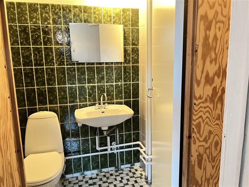 Bad med toilet, hvidt badekar, hvidt vask og spejl samt grønt og hvidt kakelbeklædt væg og gulv