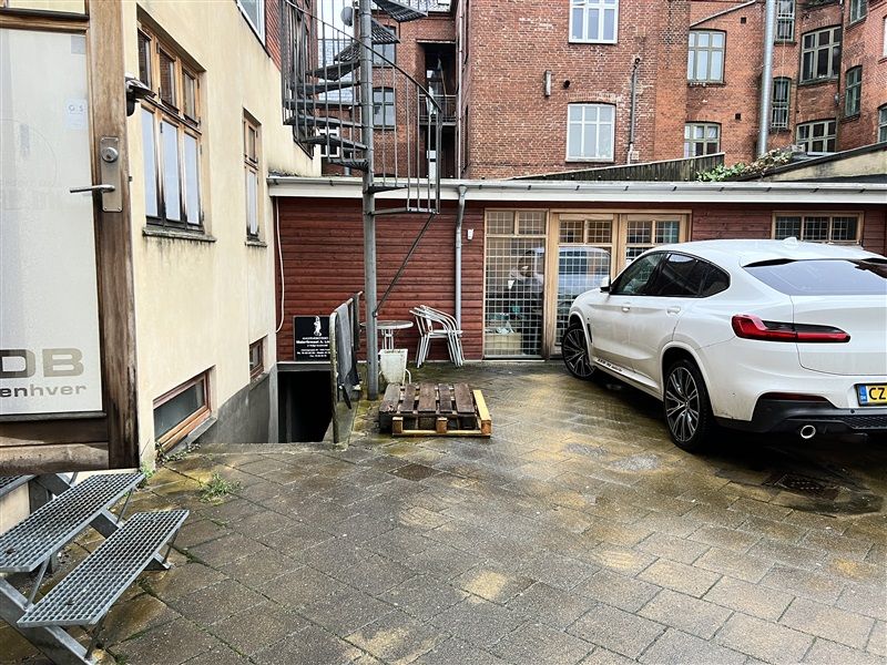 Baggård med gul stenbrolægning og parkeret hvid BMW X3 xDrive30e M Sport i baggrunden