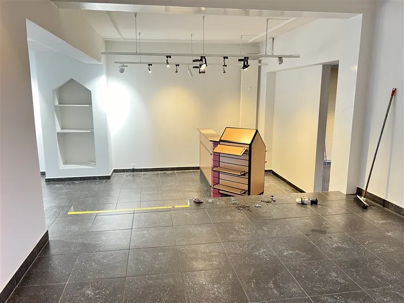 Lokal med lyse loftsbelægninger og gulvtæppe på Købmagergade 20 i Fredericia. Der er en stående hylde og et skraldespand i