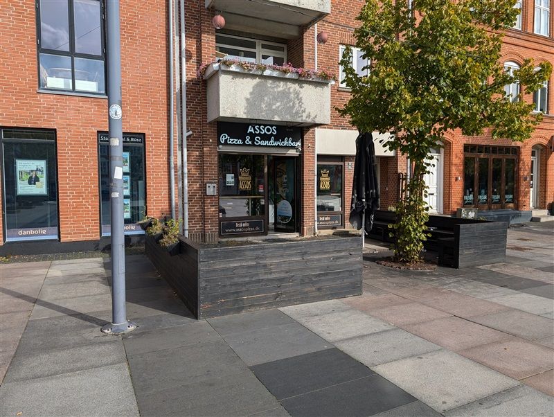 Forretningslokaler med udsigt til gågade, terrasse og planter i Fredericia. Bygningen med rød mursten og store ruder.