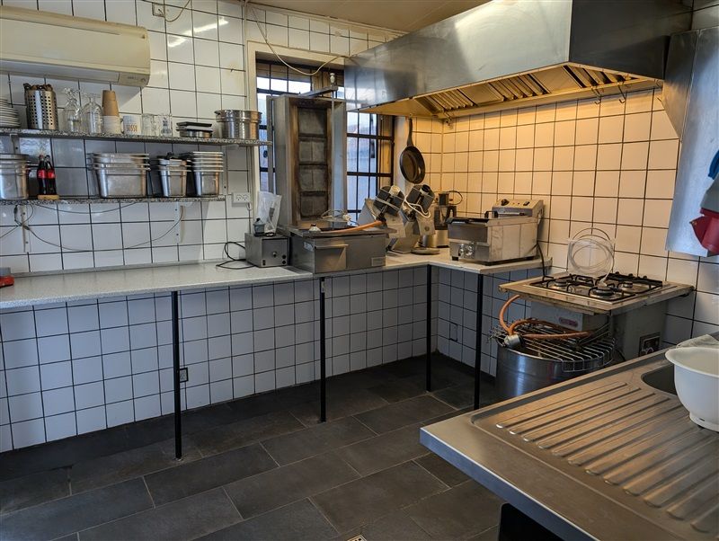 Professionelt udstyret køkken med flere kogeapparater, kogegrej, ovn og andet køkkenudstyr samt en udendørs grill