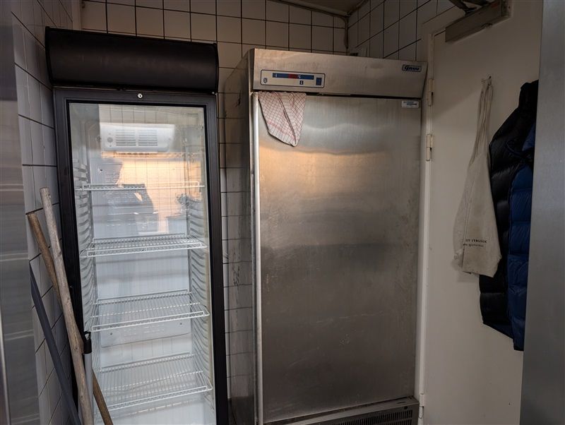 To stående køleskabe med åbne døre og en hængende hvid og blå jakke