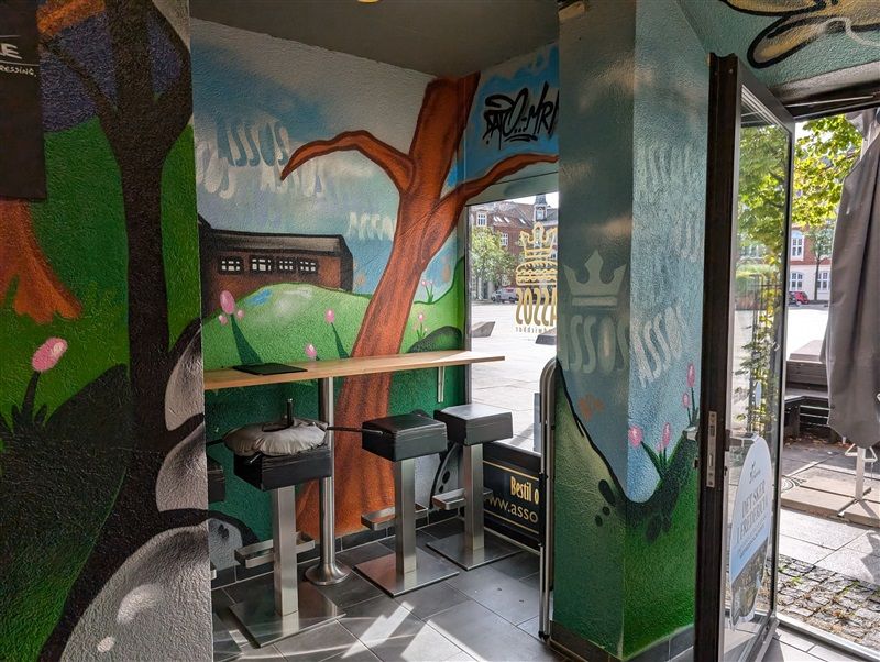 En lille café med grønne vægmaleri og tre høje stolpe med pudetopper og en bord med en tablet