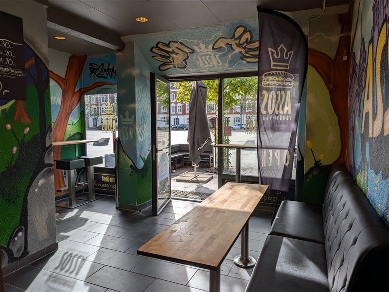 En restaurant med graffitivægge, et træbord og en sort sofa med et reklamebanner med teksten 2022 og 1910