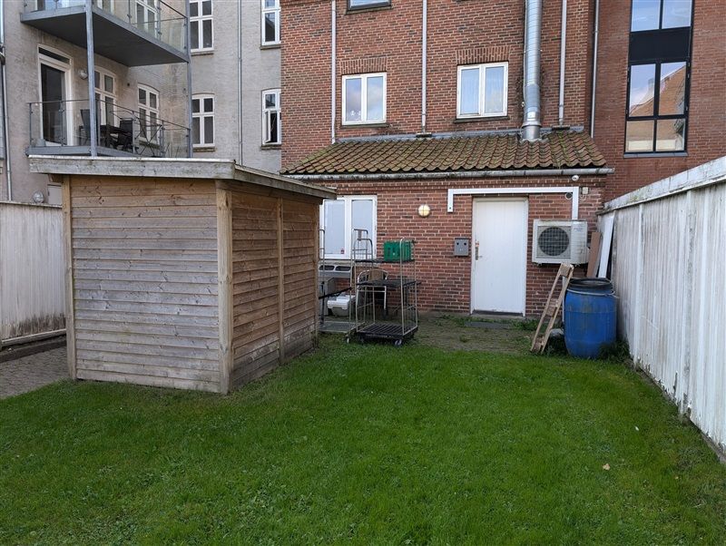 Et lille værelse med høj kælder, et skab og en køleskab, der står udenfor huset med en rullebænk og et gult skur