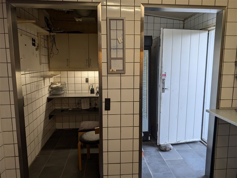 En køkken og spiseområde med køleskab, stol, servierbræt, køkkenredskaber, stol, kalender og elektriske ledninger