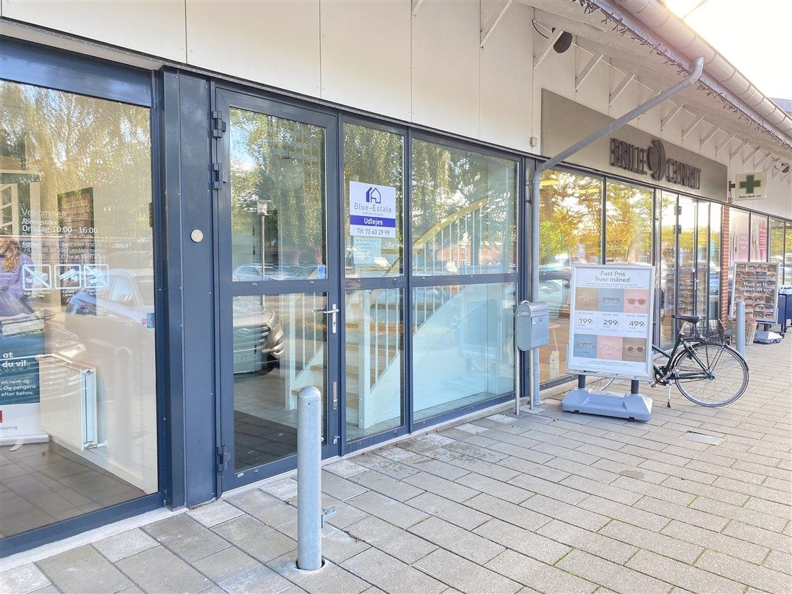 udenfor Blue-Estate Ejendomsmæglerforretning. Et cykelstativ står udenfor døren, hvor man kan se, at lokalerne er åbne.