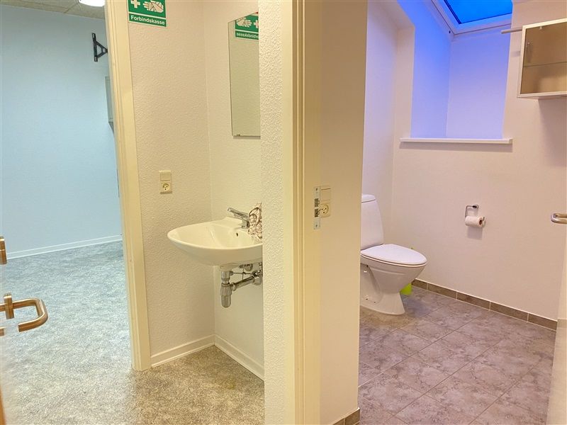 Et lille badeværelse med et toilet, en hvid vask og et spejl samt gulv og vægge med mønstret udseende