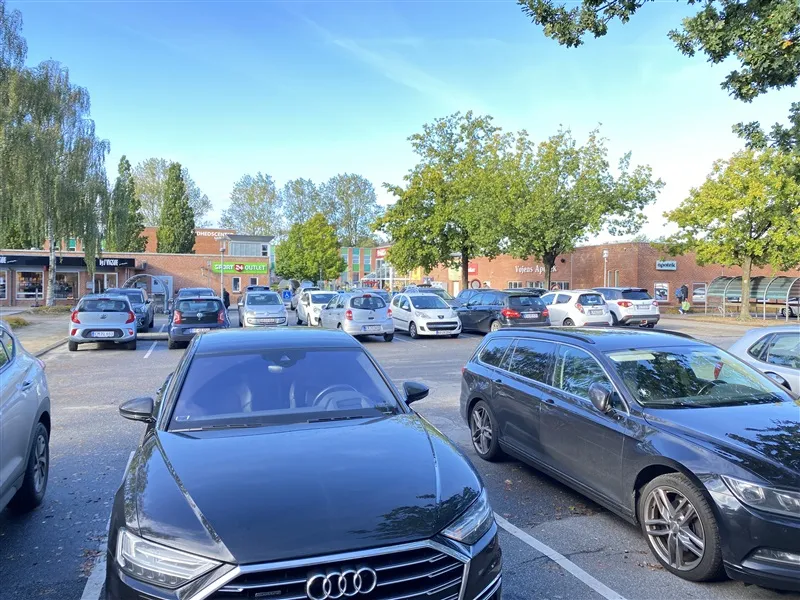 Mange biler parkeret på parkeringsplads ved Rådhuscentret i Vojens, med tredje generationens Audi A7 og Audi Q7.