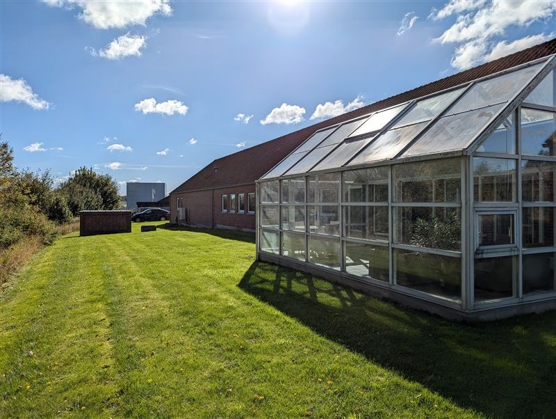 Et moderne jordbrugsglashus med solceller på taget står på en grøn plæne i en solrig dag