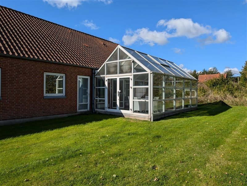 Et hus med en altan og en terrasse, der er fuld af glas, og en græsplæne med røde mursten
