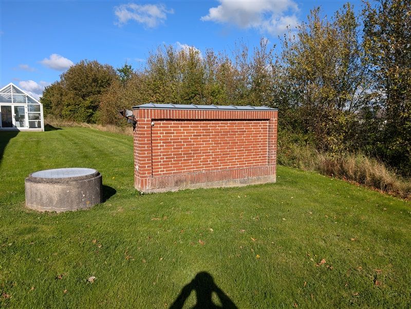 Rød murstensbygning med grå tagplade og et kamera monteret på væggen uden foran en græsplæne med en stenrundning og en