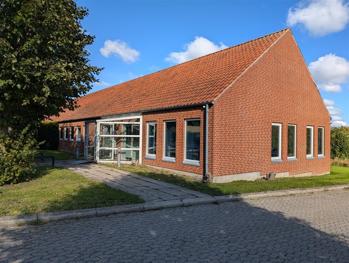 Nybygget erhvervsejendom med røde mursten, glasvinduer og en terrasse i skovsiden. Bygmestervej 29, 5750 Ringe.