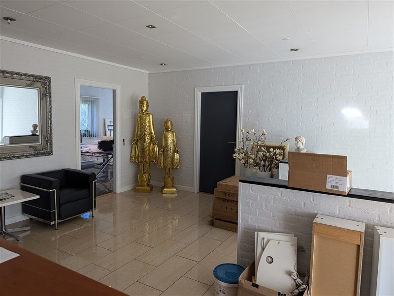 Inde i lokaler med hvide vægge og gulv er der to store guldfarvede statuer og en hvid vase med blomster