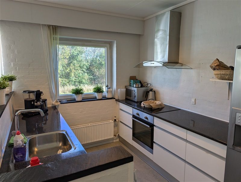 En moderne køkken med lyse møbler, en høj ovn og en spisestue med vinduer og plantepotte