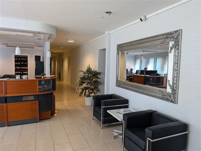 En elegant lobby med hvide vægge, to sort læderstole og et stort spejl med sølvfarvet ramme