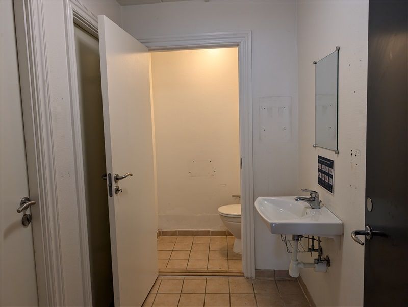 Hjørne af et lille badeværelse med toilet, håndvask og spejl på væggen