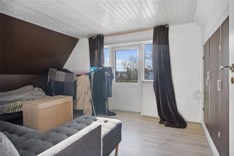 Lille værelse med højloft, hvidt loft og vægge, gulvbelægning, sofa, seng, tøjstativ og to hængekurve med tøj